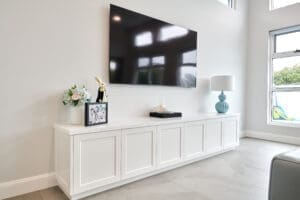An inviting white living room with an entertainment unit and a wall-mounted flat screen TV, perfect for relaxation and entertainment.